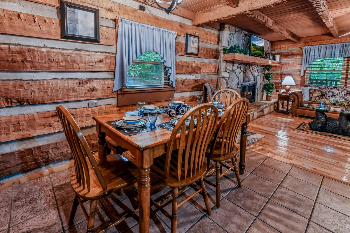 A spacious dining area with a large wooden table set near a stone fireplace and surrounded by comfortable seating and decorative windows. The space invites guests to gather for meals, play games, or simply unwind together.
