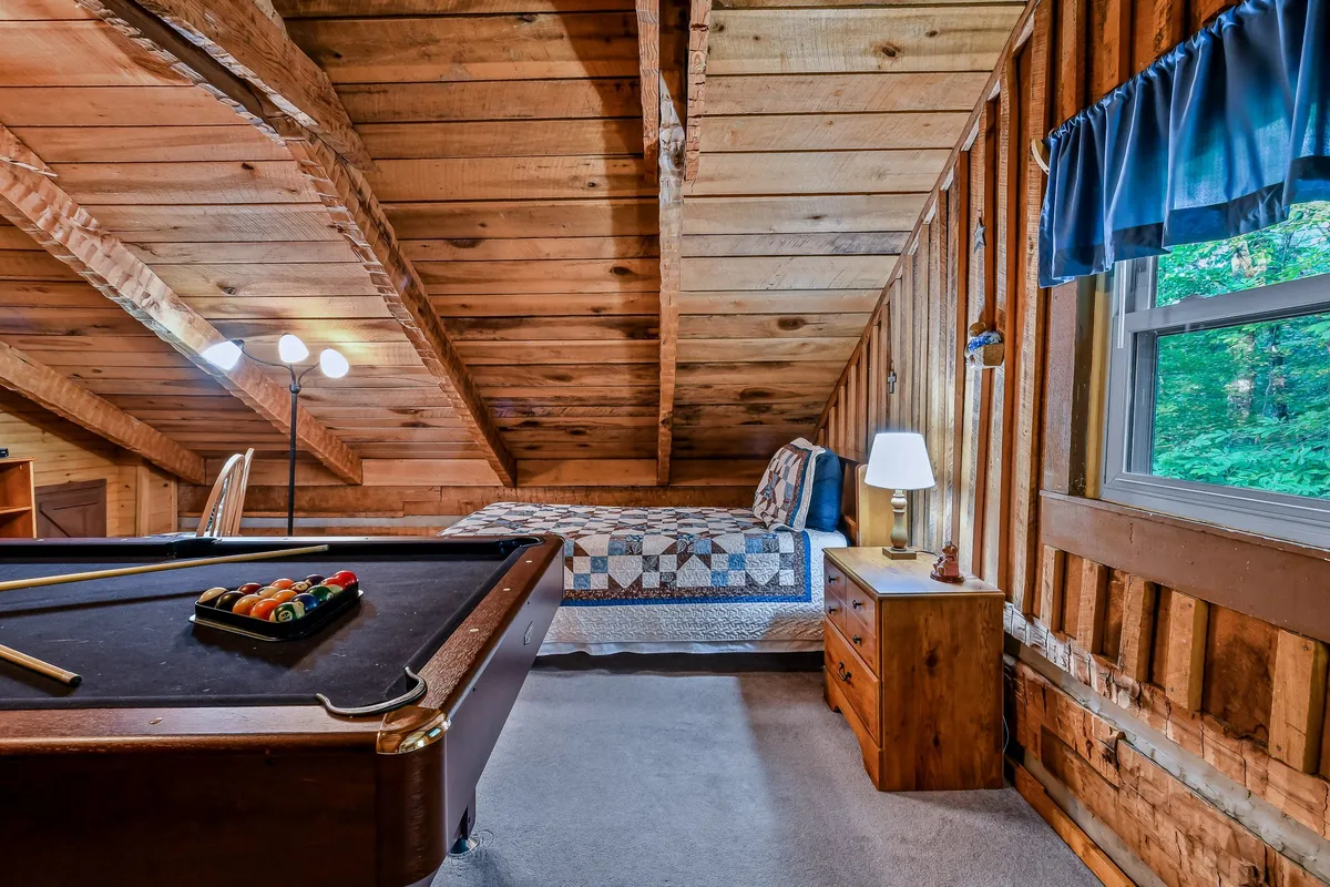 Inside, this image highlights the game room area with a pool table, bed, lamp, and wooden walls. The playful, inviting mood showcases a key indoor entertainment space, echoing the section’s mention of the upstairs game room with games and sleepover vibes—ideal for rainy days or family downtime.