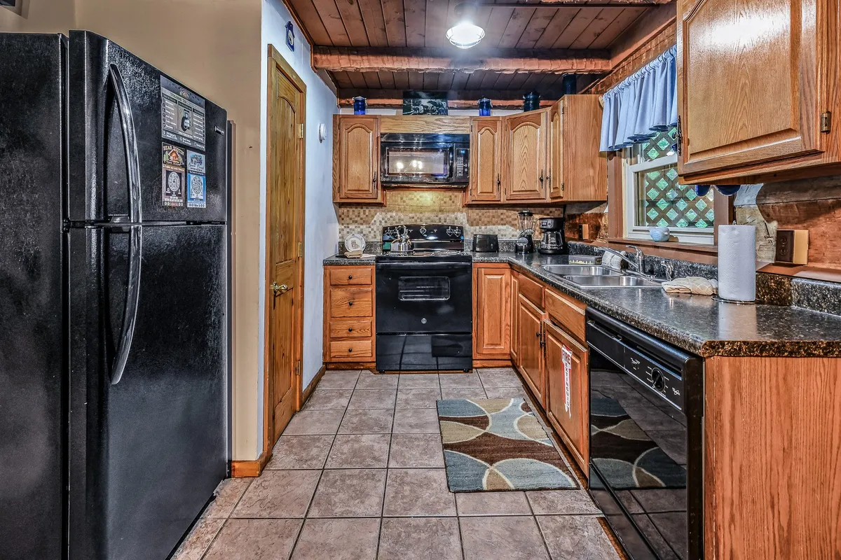 A modern, fully equipped kitchen with wooden cabinets, granite countertops, a black refrigerator, oven, and a sink. The layout provides ample space for cooking and socializing, fostering culinary creativity and togetherness.