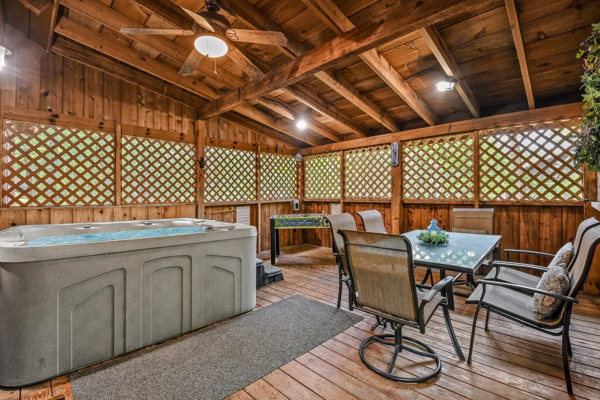 This interior image showcases a tranquil hot tub area with a view of a dining table, wooden ceiling, and lattice windows. The hot tub is the focal point, surrounded by inviting seating, ideal for relaxation and social gatherings.