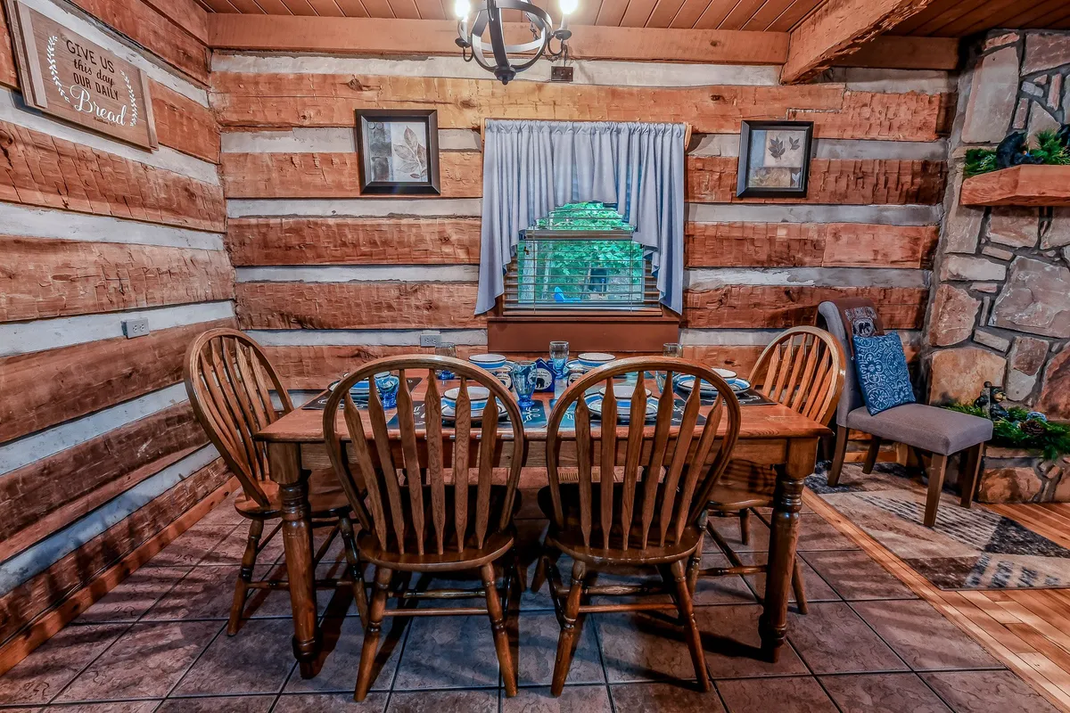A spacious open dining area with a wooden table and matching chairs, set beside a stone fireplace and large curtained window. The setting is ideal for family dinners, game nights, and group celebrations.