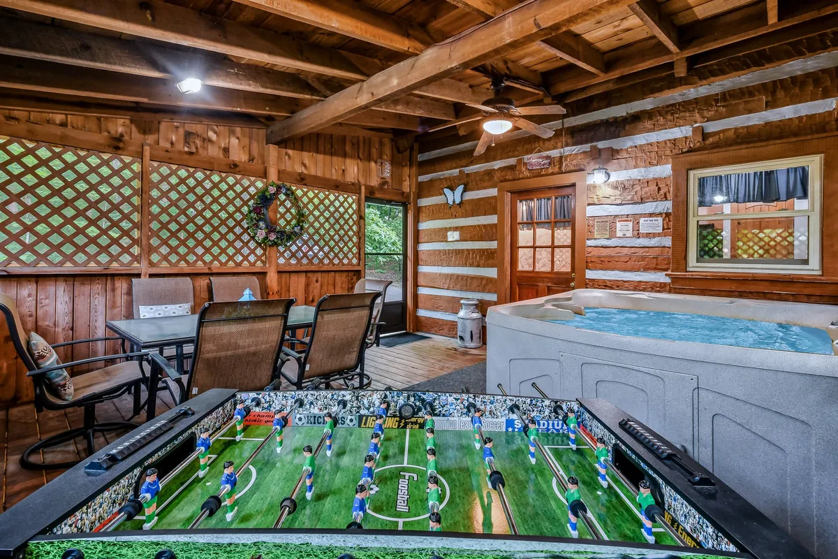 A foosball table stands ready for action in a spacious, casual area that also includes a hot tub, dining area, and rustic wooden beams. The playful scene hints at lively gatherings and multiple options for entertainment.