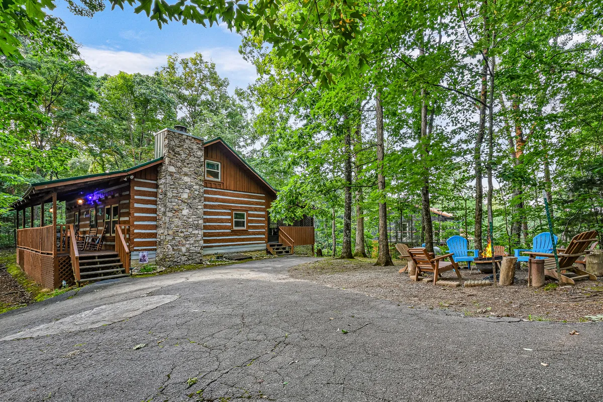 A log cabin exterior featuring a spacious outdoor seating area, a prominent fire pit, and a stone chimney. The scene is set for family gatherings, outdoor barbecues, and evenings by the fire under the stars.