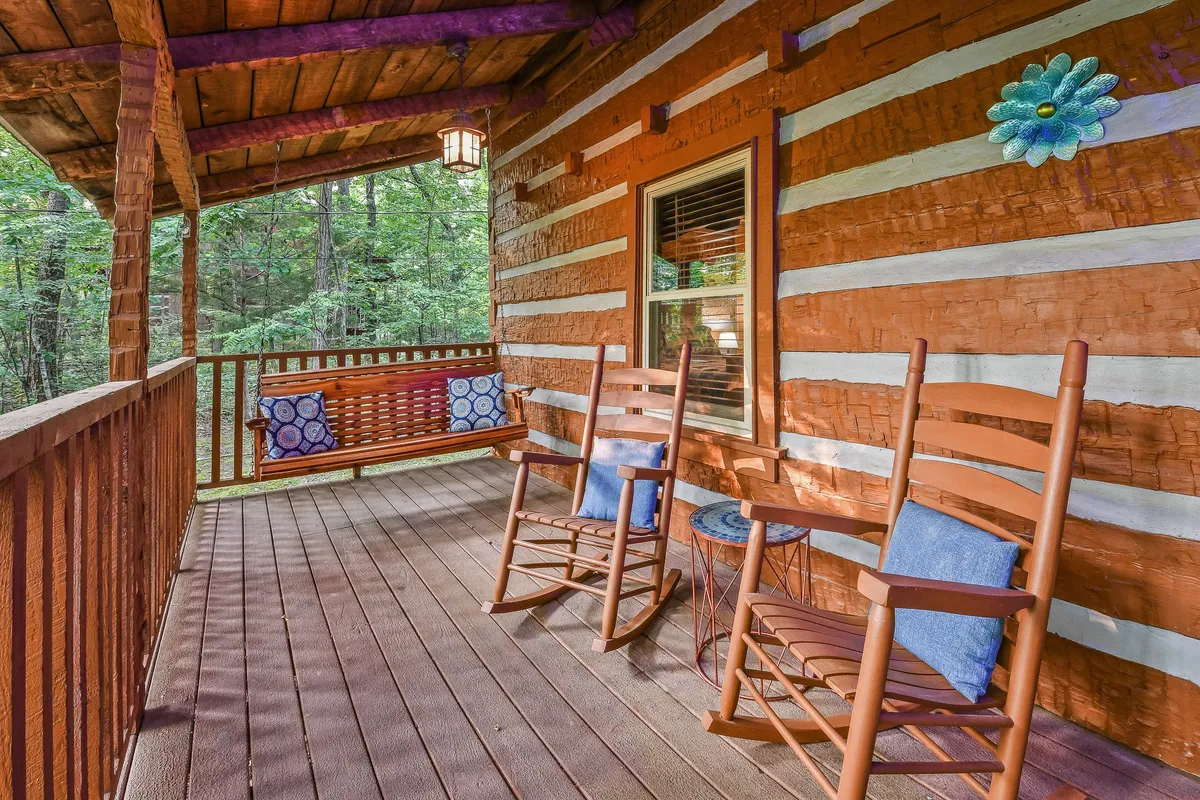 An exterior porch scene with rocking chairs and a swing bench, accented by decorative flowers and rustic wooden beams. The area exudes a cozy and inviting atmosphere, perfect for enjoying nature and unwinding.