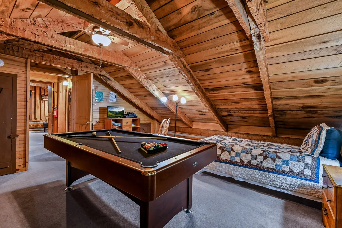 A playful game room setup with a billiard table, a quilted bed nearby, and exposed wooden beams above. The room is designed for both friendly competitions and laid-back relaxation, encouraging social interaction among guests.