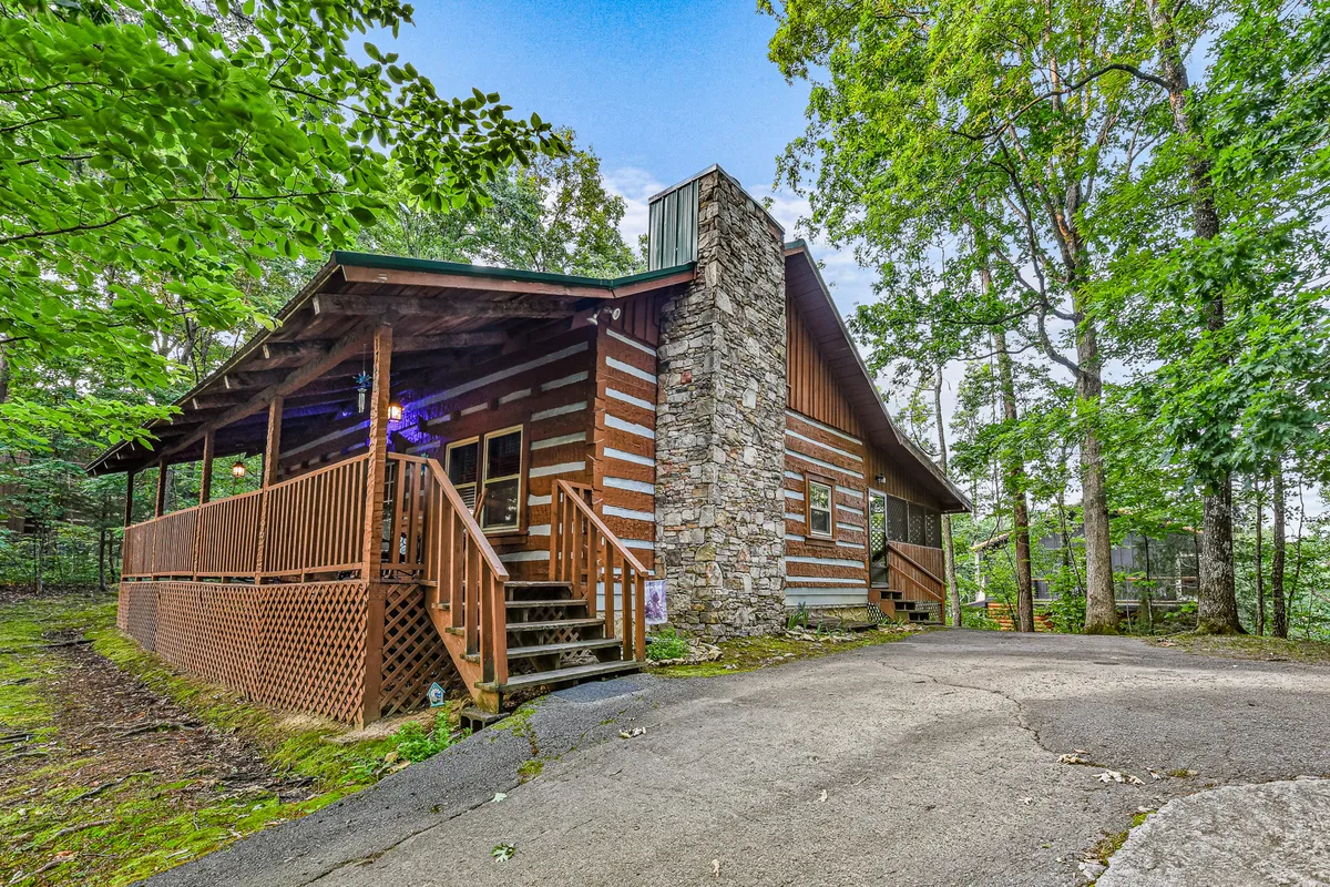This image showcases the exterior of the log cabin, highlighting its stone chimney, welcoming wooden porch, and the surrounding lush trees. The scene exudes a cozy and serene mood, perfect for family gatherings, relaxing outdoors, and connecting with nature. The porch space hints at stargazing and gathering around the fire pit—activities directly referenced in the section.