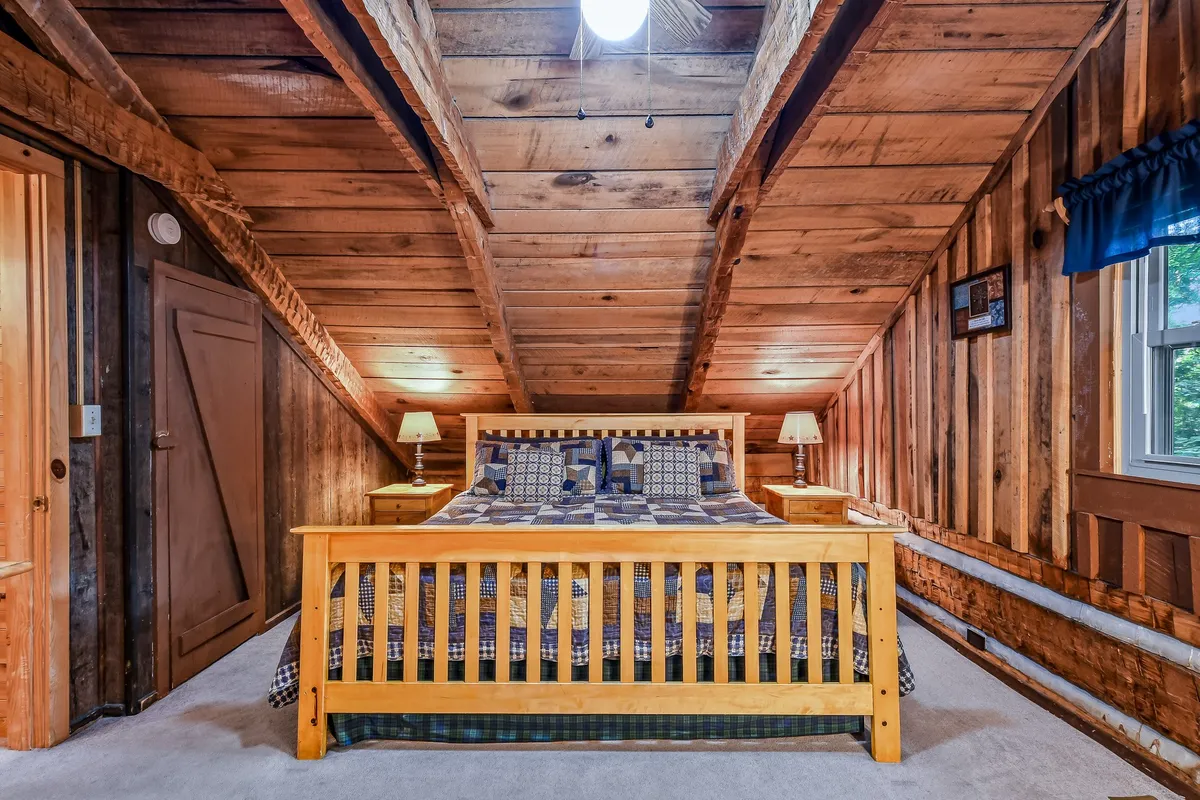 A warmly lit bedroom featuring a wooden bed with inviting plaid bedding, rustic wooden beams, paneled walls, and nightstands. The room exudes comfort with sunlight streaming in, suggesting a cozy retreat perfect for restful sleep after a day of adventure.